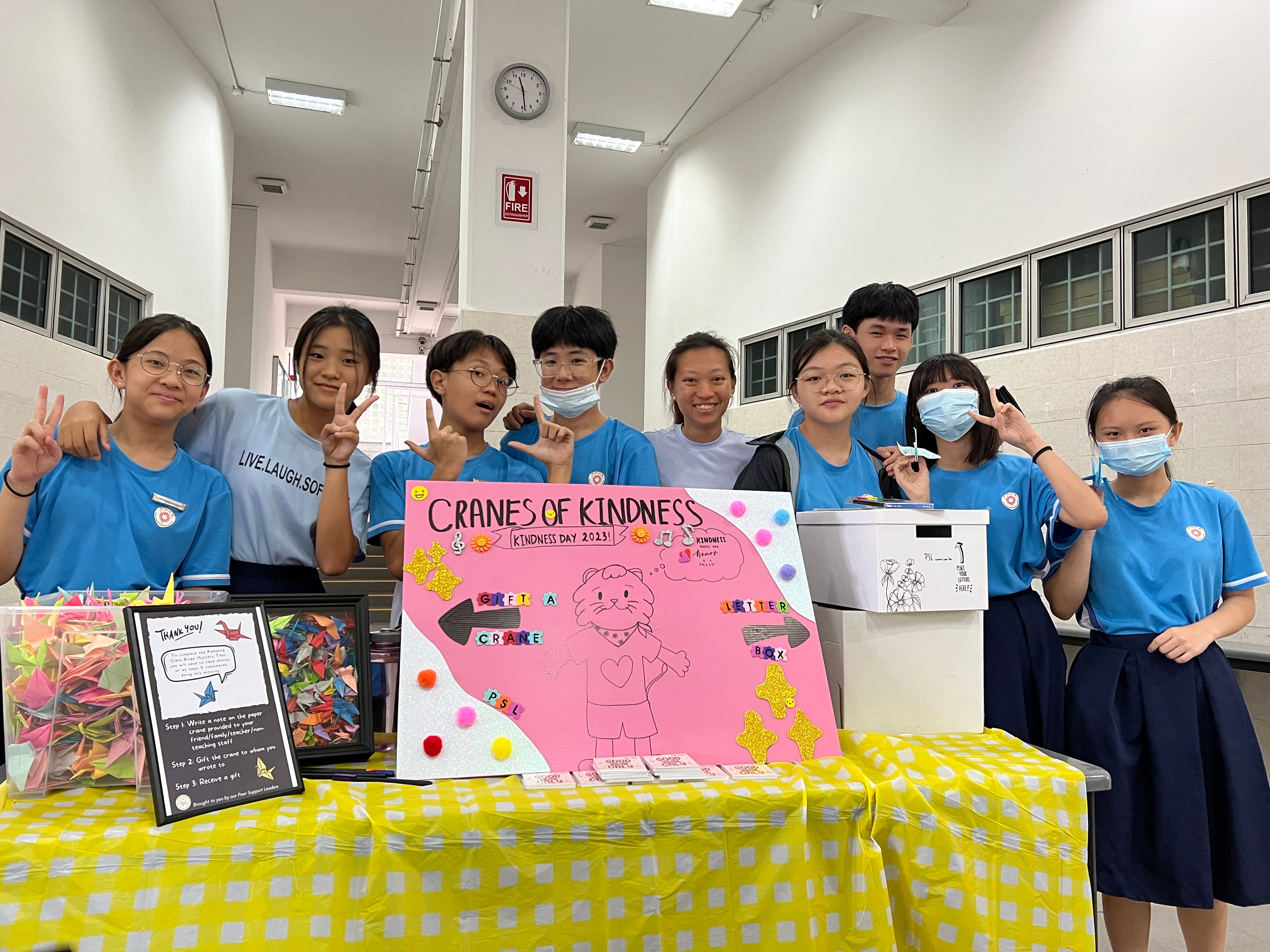 A group of students standing behind a booth setup in the canteen, promoting kindness towards each other.
